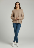Woman wearing a beige sweater and blue jeans on a plain background
