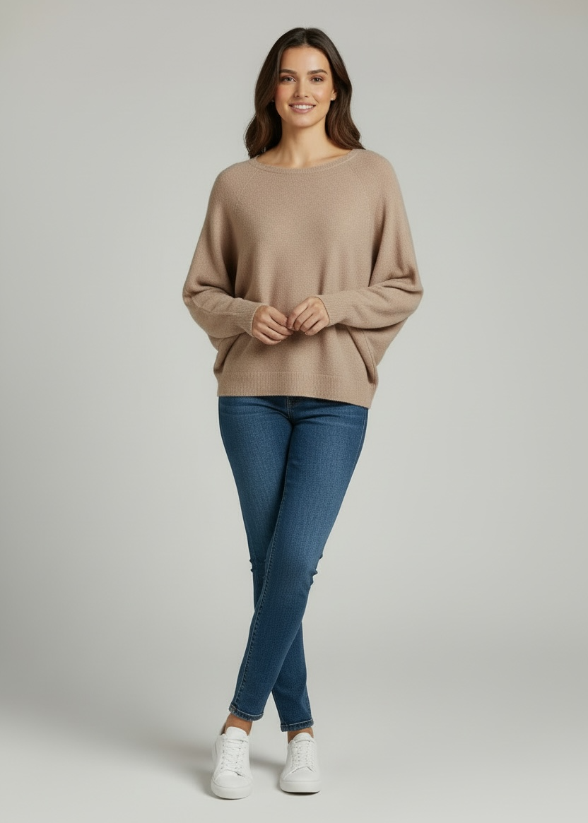 Woman wearing a beige sweater and blue jeans on a plain background