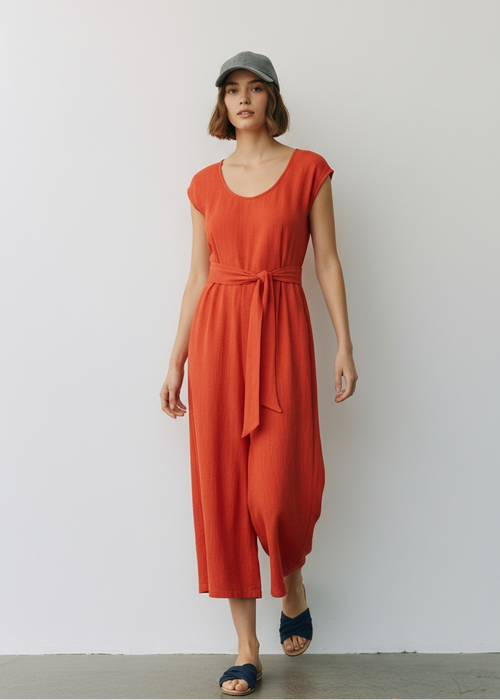 Woman wearing an orange dress and cap against a white wall