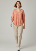 Woman wearing a coral blouse and beige pants on a plain background