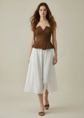 Woman wearing a brown peplum top and white skirt on a beige background