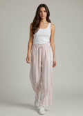 Woman wearing a white tank top and pink striped pants on a plain background