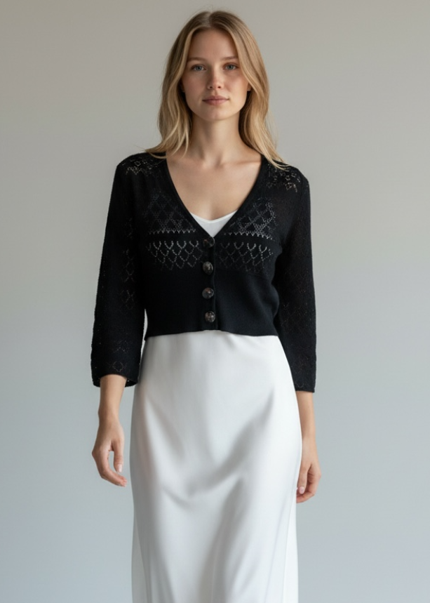 Woman wearing a black cardigan, white skirt, and white shoes on a plain background