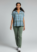 Woman wearing a blue plaid shirt and green pants on a gray background