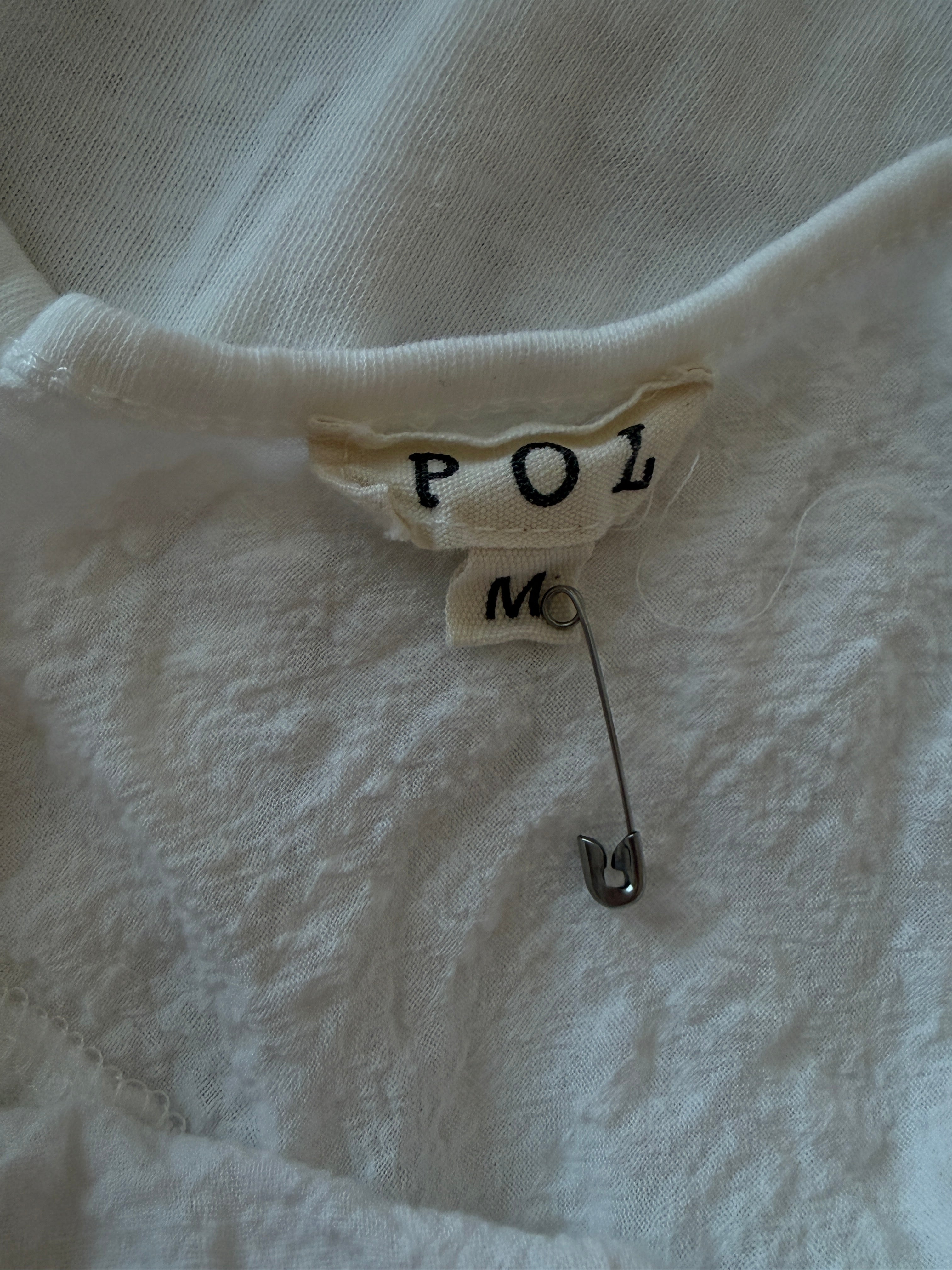 Close-up of a white garment with a label and safety pin on a textured white background