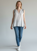 Woman wearing a white sleeveless top with black lace details and blue jeans on a plain background