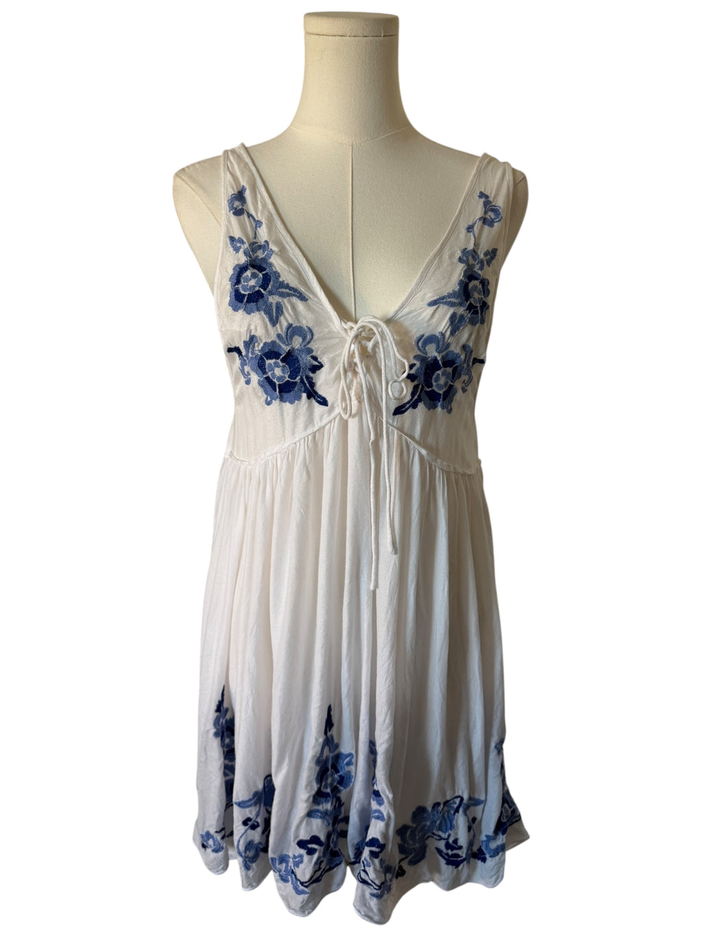White dress with blue floral embroidery on a mannequin against a white background