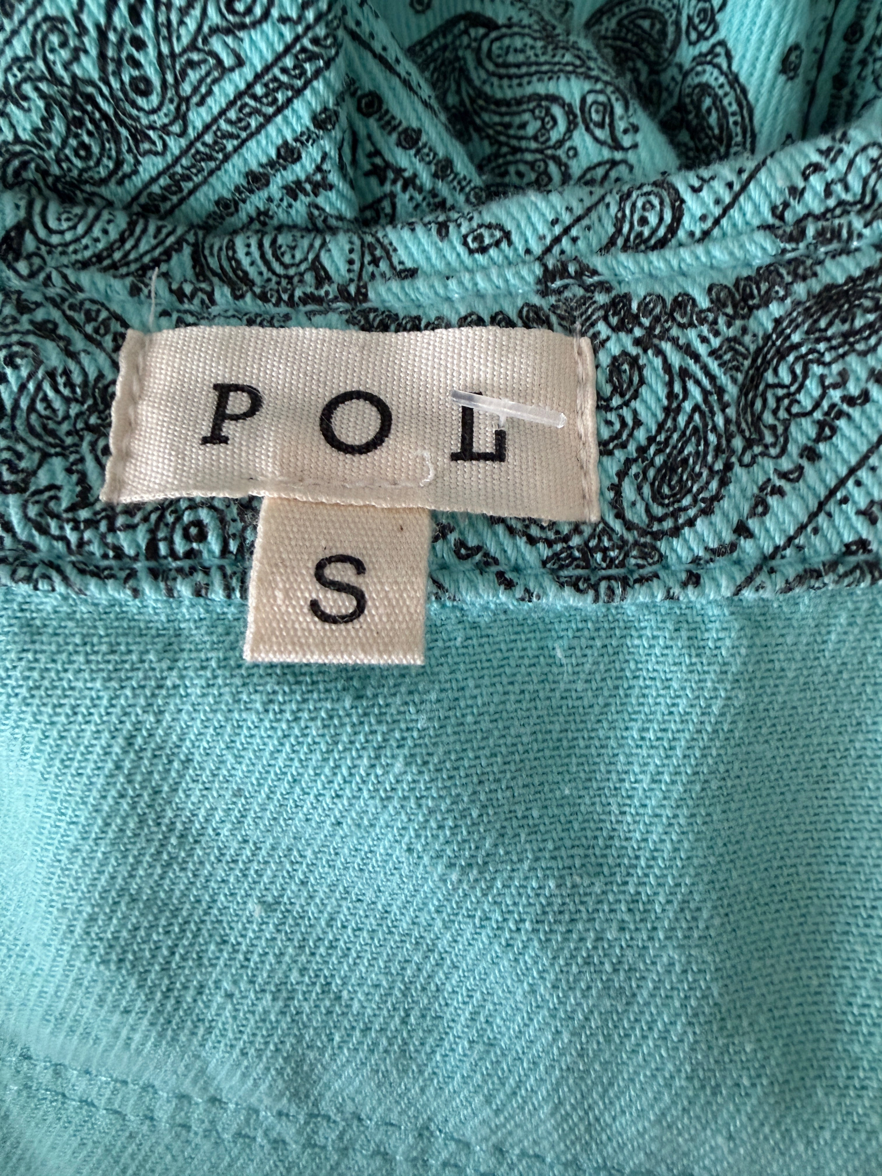 Close-up of a turquoise fabric with a patterned label displaying 'POL S'.