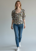 Woman wearing a floral blouse and blue jeans against a plain background