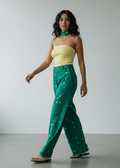 Woman wearing a yellow top and green pants against a plain background