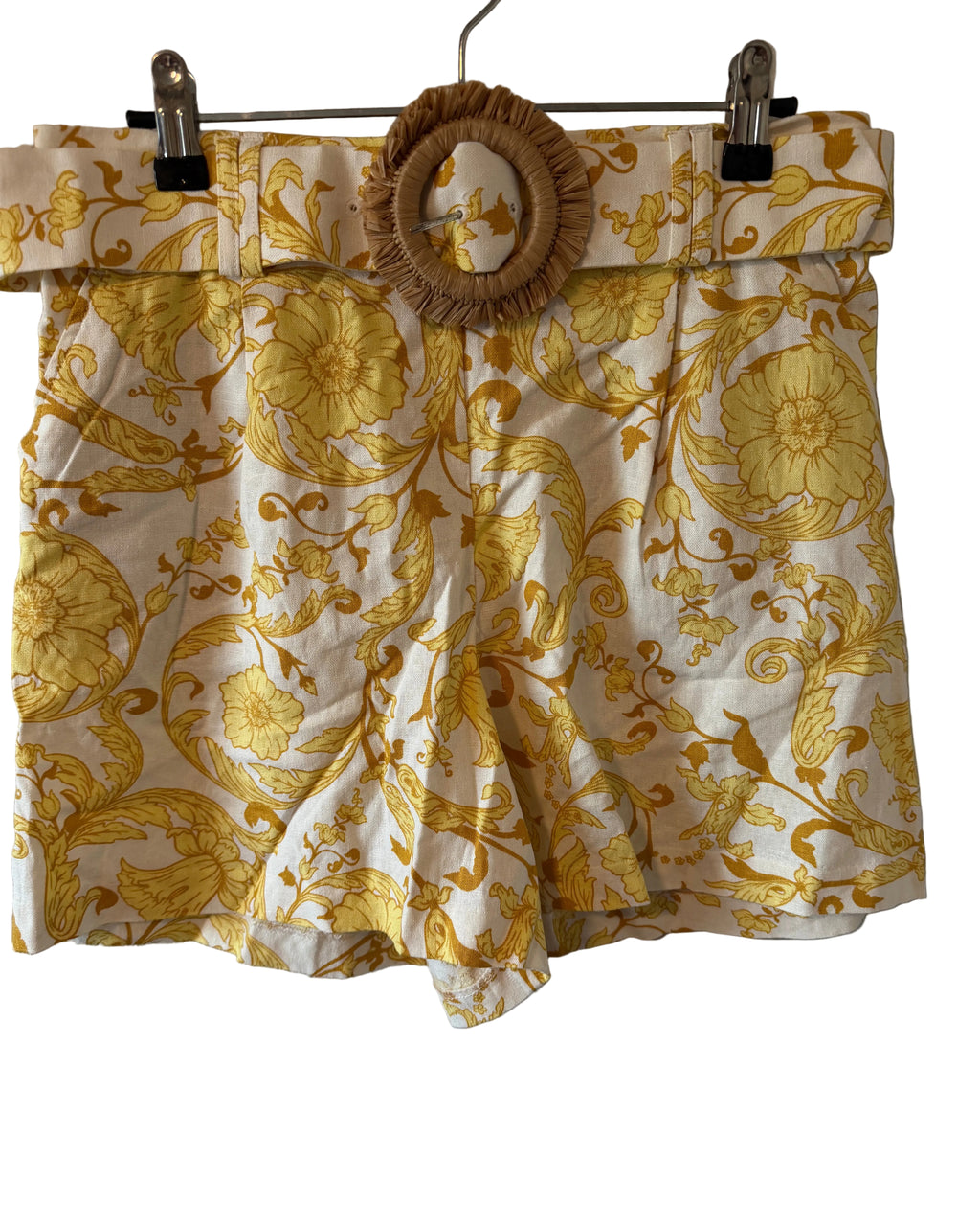 Yellow floral shorts hanging on a rack against a plain wall.