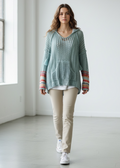 Woman wearing a light blue knitted hoodie with a colorful patterned scarf in a minimalistic room.