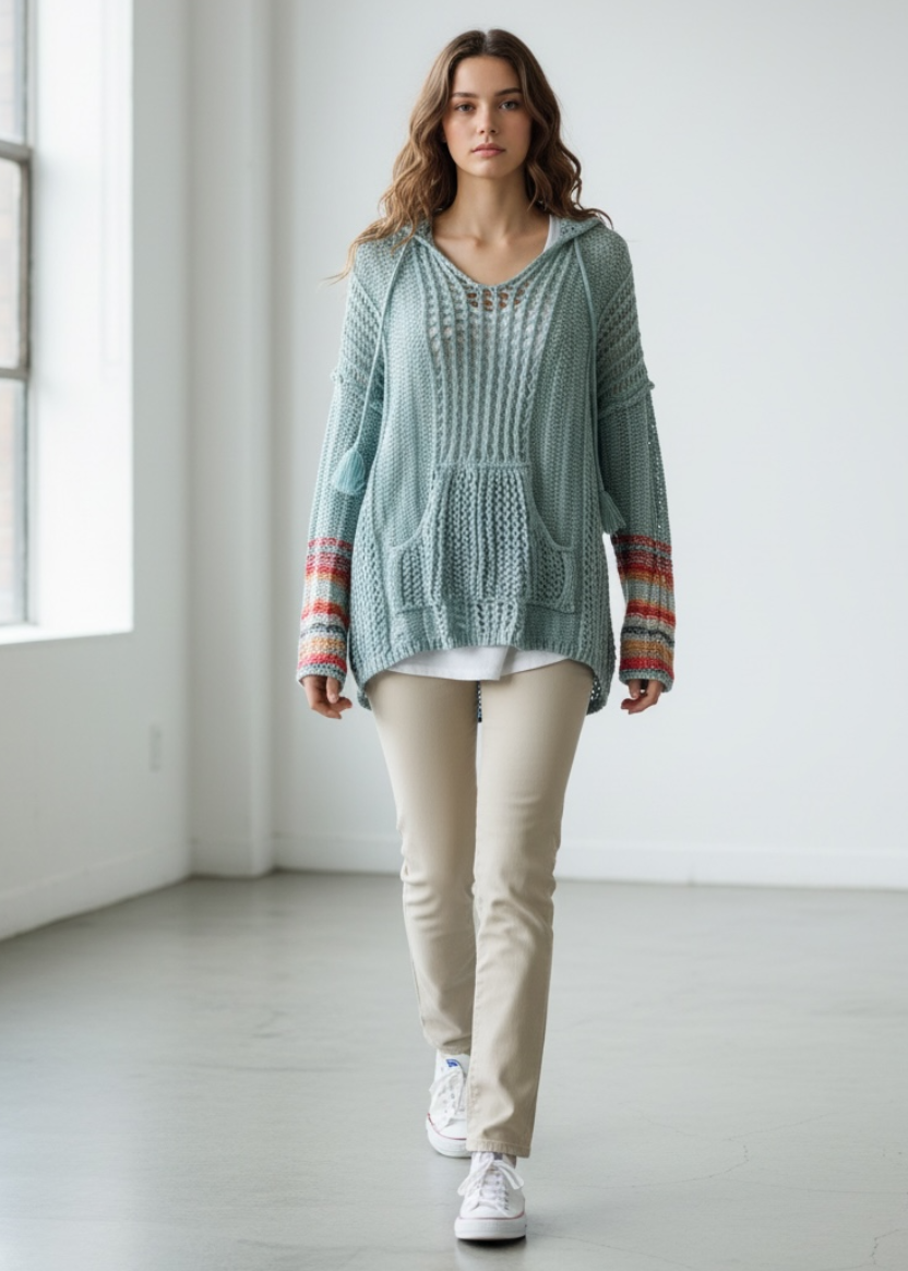 Woman wearing a light blue knitted hoodie with a colorful patterned scarf in a minimalistic room.
