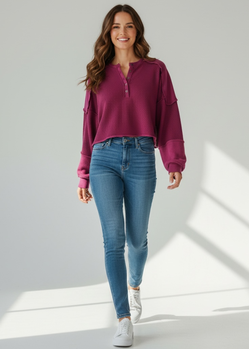 Woman wearing a purple sweater and blue jeans standing in a well-lit room.