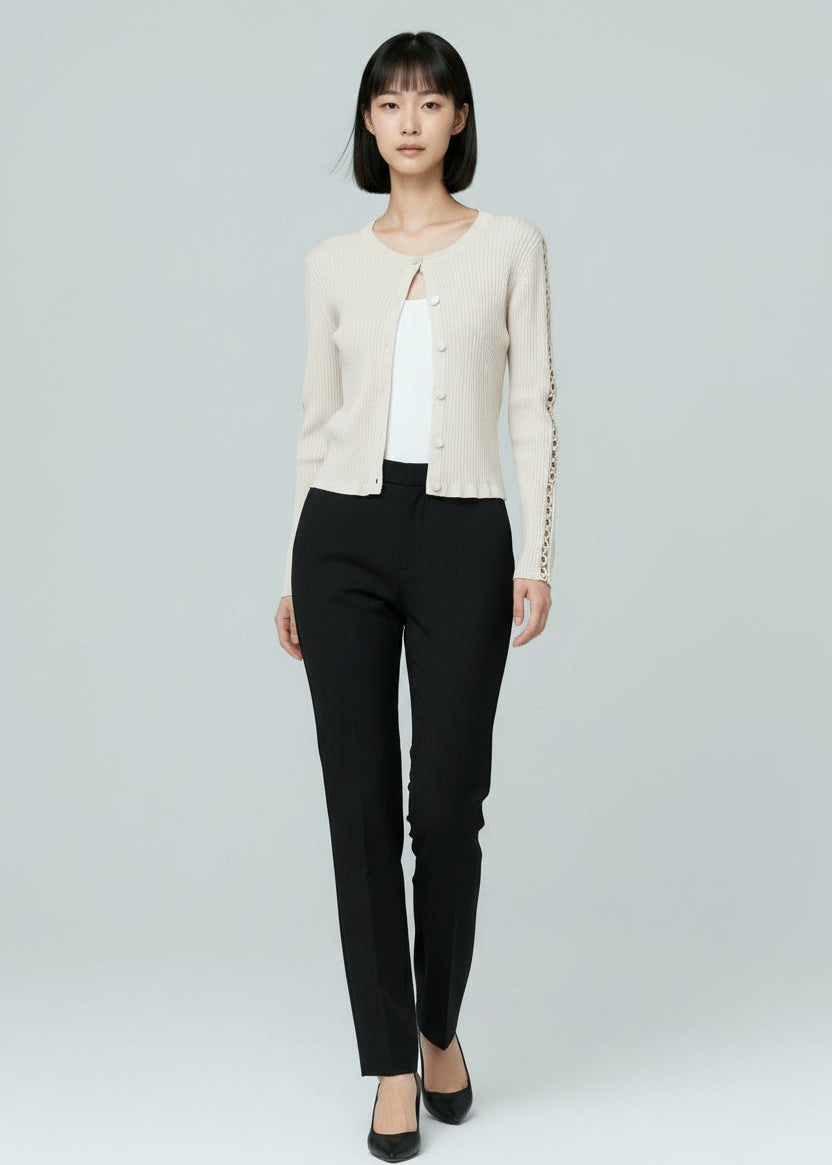Woman wearing a white cardigan, white top, black pants, and black shoes on a light gray background