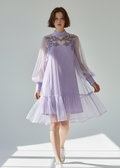 Woman wearing a light purple dress with sheer sleeves on a gray background