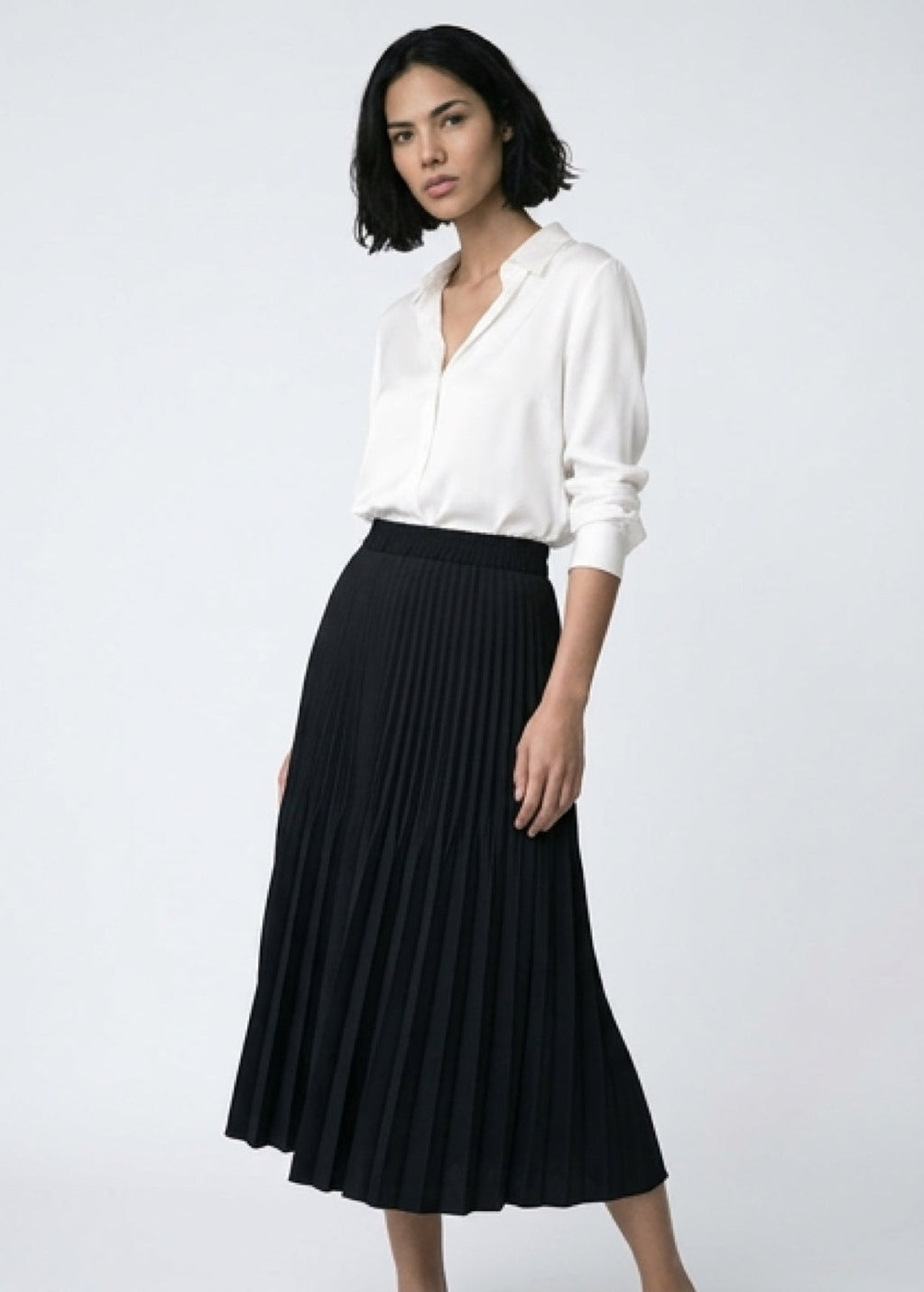 Woman wearing a white blouse and black pleated skirt on a white background