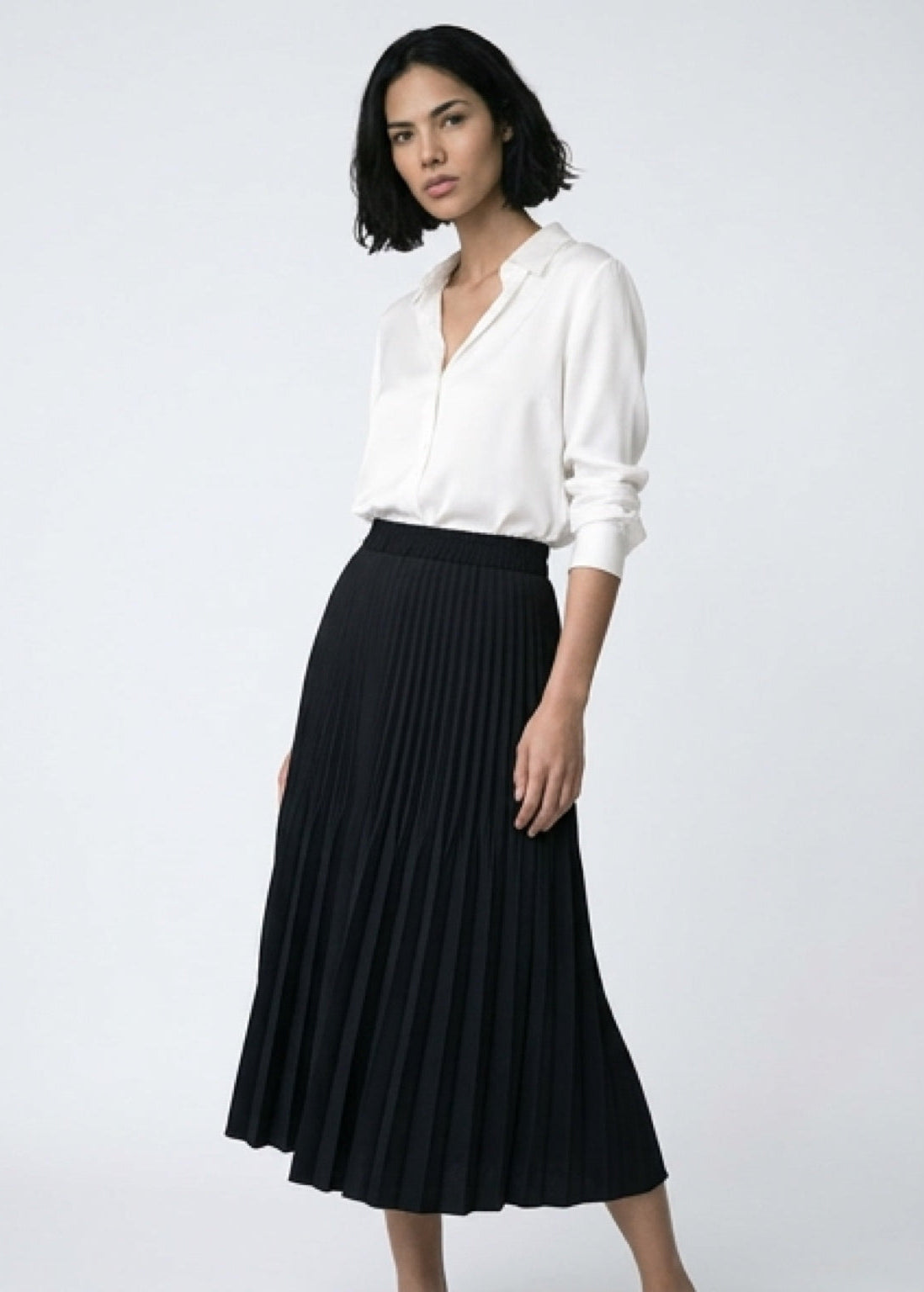 Woman wearing a white blouse and black pleated skirt on a white background