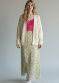 Woman wearing a pink top, cream cardigan, and floral skirt against a plain background
