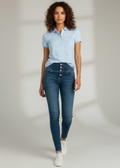 Woman wearing a light blue polo shirt and dark blue jeans on a plain background