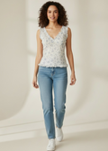 Woman wearing a floral sleeveless top and light blue jeans on a beige background