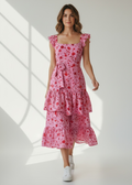 Woman wearing a pink floral dress standing in a well-lit room with sunlight filtering through.