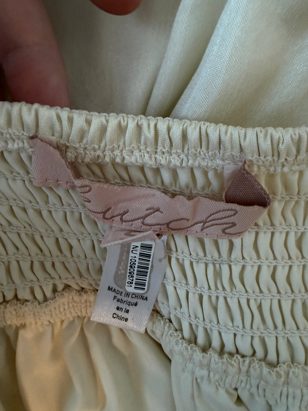 Close-up of a textured fabric with a brand tag attached, showing visible stitching details.