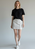 Woman wearing a black t-shirt and white skirt with white sneakers on a plain background