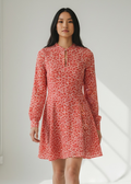 Woman wearing a red floral dress standing in a bright room with white walls and floor.