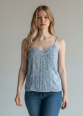 Woman wearing a light blue patterned tank top and blue jeans against a plain background