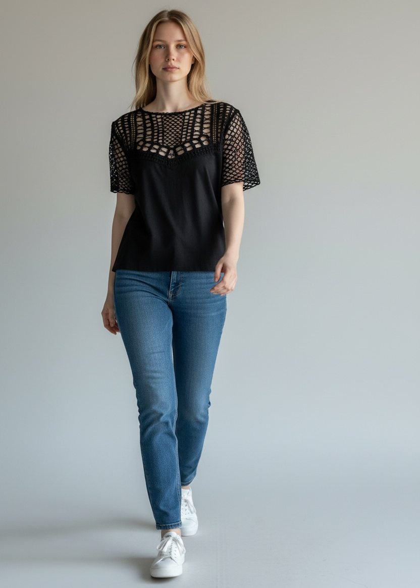Woman wearing a black top with lace details and blue jeans on a plain background