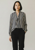 Woman wearing a striped blouse and black pants against a plain background