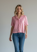 Woman wearing a pink Sequin shirt and blue jeans against a plain background